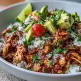 Tender shredded salsa chicken served over rice with black beans, corn, avocado, and a sprinkle of cheese and cilantro.  