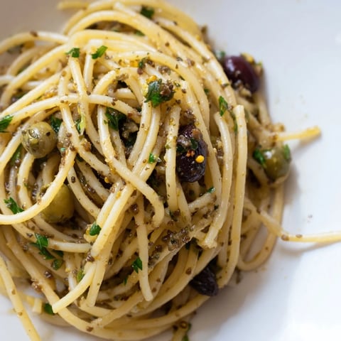 Steaming bowls of olive tapenade pasta, featuring a chunky, briny sauce of olives and capers over al dente spaghetti, garnished with fresh parsley and lemon zest.