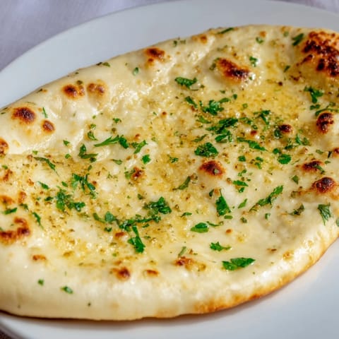 Freshly baked garlic naan, featuring blistered spots and a fragrant, buttery garlic finish.