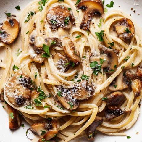 A serving of creamy mushroom linguine rests beside a glass of white wine and fresh parsley garnish.  