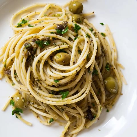 A close-up of olive tapenade pasta tossed in a vibrant green olive and caper sauce, with grated Parmesan and fresh parsley for a Mediterranean-inspired main dish.