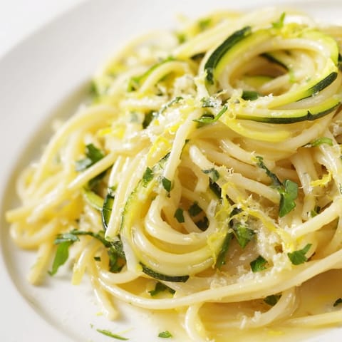A fork twirls into a bowl of Lemon Zucchini Pasta, highlighting al dente spaghetti and crisp zucchini ribbons next to a glass of crisp white wine.  