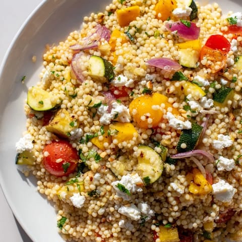 A vibrant bowl of Roasted Veggie Couscous Salad, garnished with feta, mint, and toasted pine nuts.  