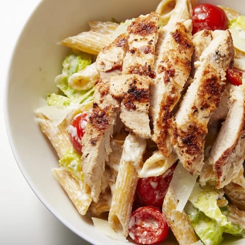 A close-up of the Spicy Chicken Caesar Pasta bowl, featuring sliced grilled chicken, crisp lettuce, and cherry tomatoes.  