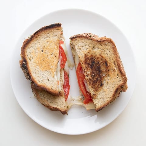Freshly made Pepper Jack & Tomato Grilled Cheese on a wooden cutting board, golden-brown bread with pepper jack cheese and ripe tomato slices.  