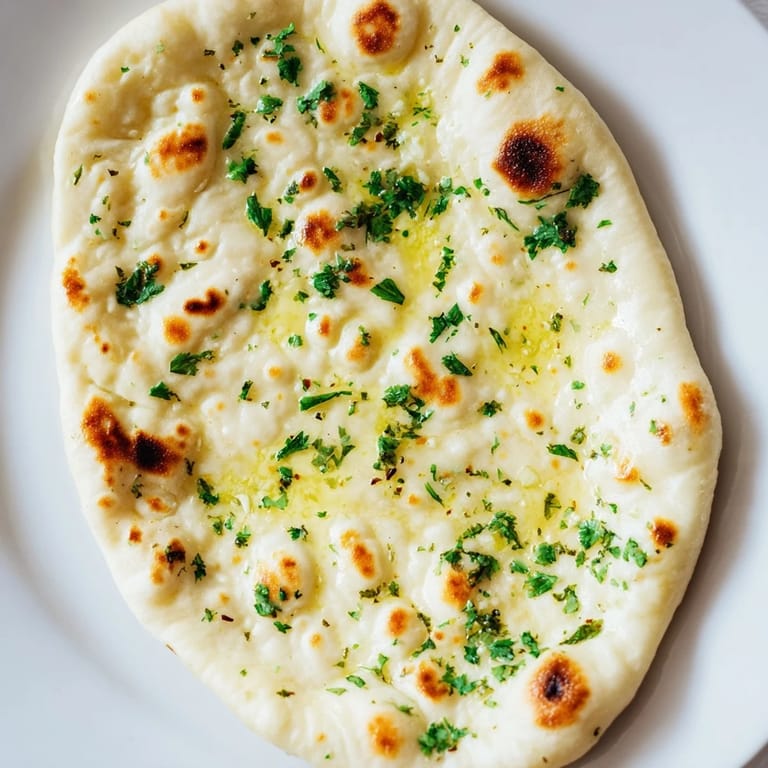 Image of warm, soft homemade garlic naan, invitingly displayed near a bowl of curry.