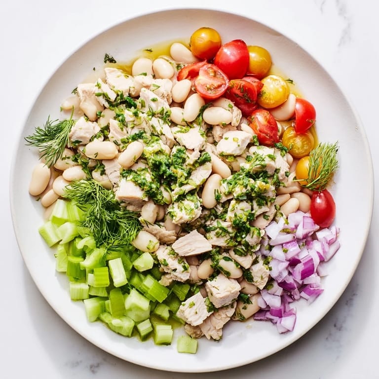 A close-up of Lemony White Bean Chicken Salad showing cherry tomatoes, red onion, and dill on a platter, perfect for a light lunch.