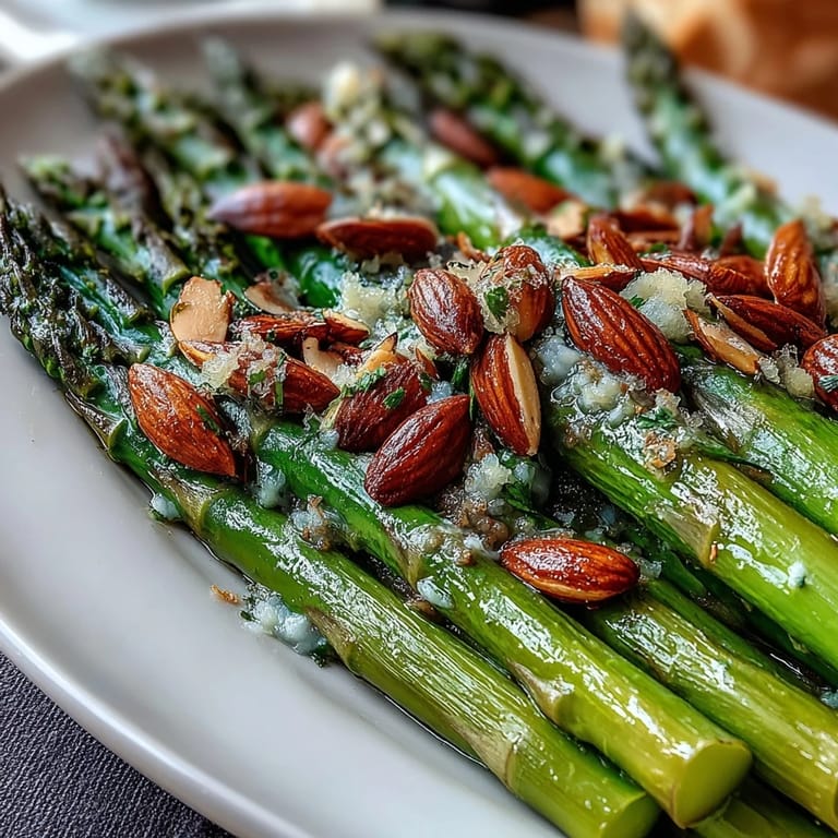 Lemon butter asparagus with almonds served on a white platter, showcasing bright green spears and golden toasted nuts.