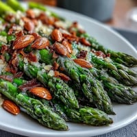 Vibrant asparagus spears glistening with lemon butter, topped with toasted almonds for a fresh, crunchy side dish.